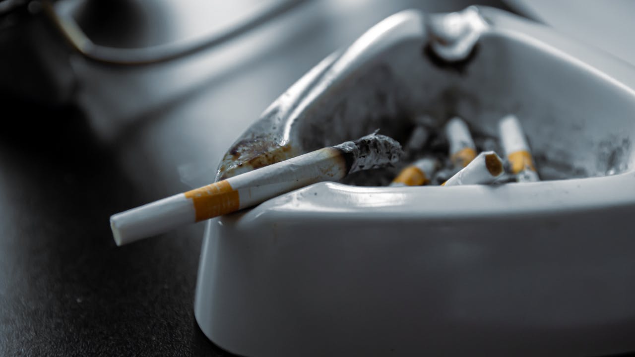 why-choose-us A close-up shot of a white ashtray filled with used cigarettes on a dark surface.