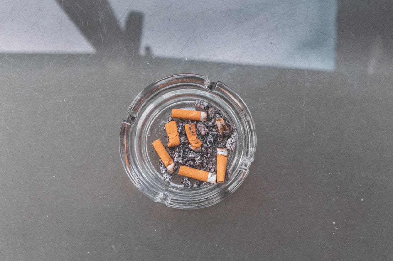 gallery-1 Close-up view of a glass ashtray filled with cigarette butts, emphasizing smoking and litter issues.