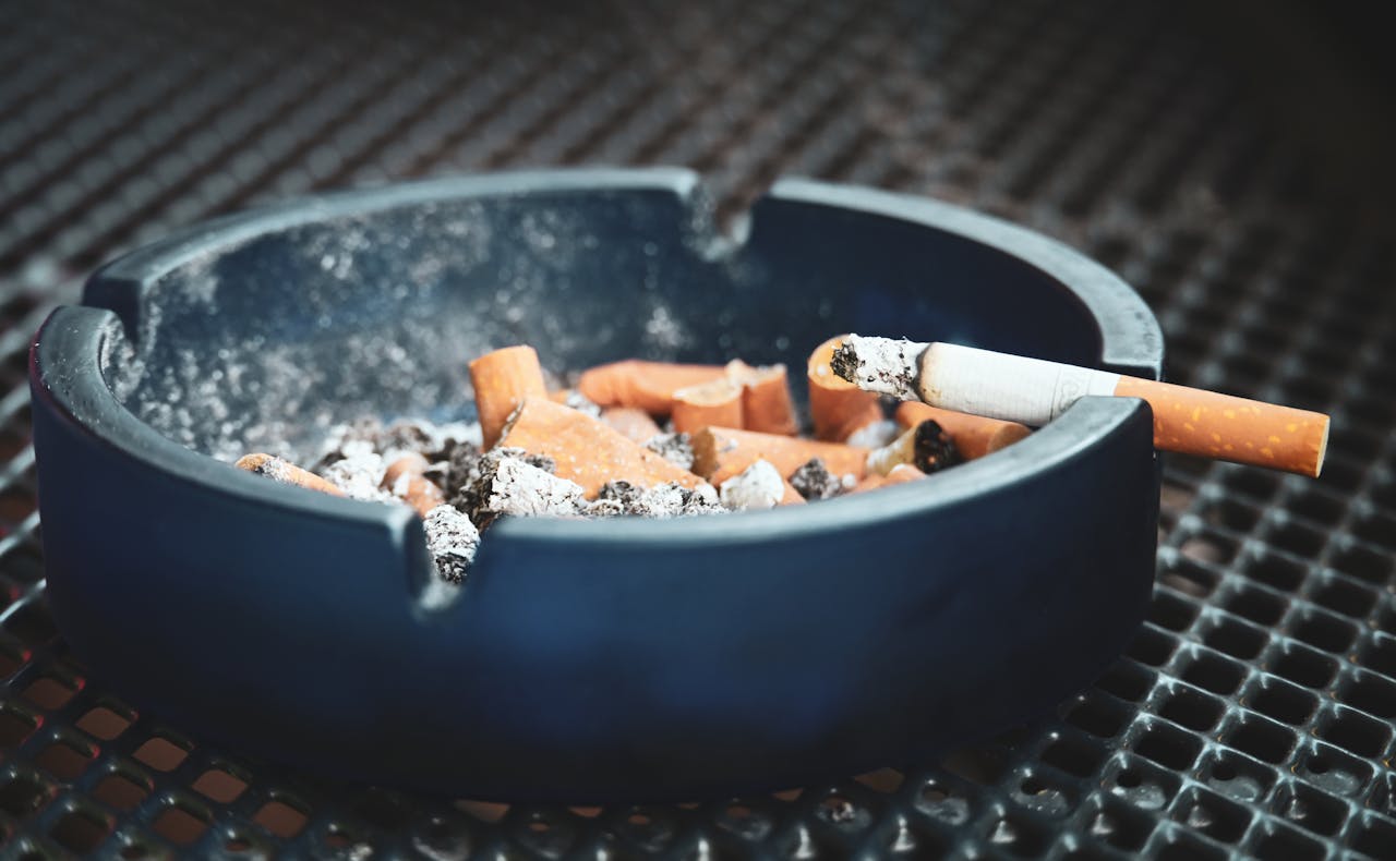 about-01 Close-up of cigarette butts and ashes in a blue ashtray with a smoldering cigarette, highlighting smoking habits.