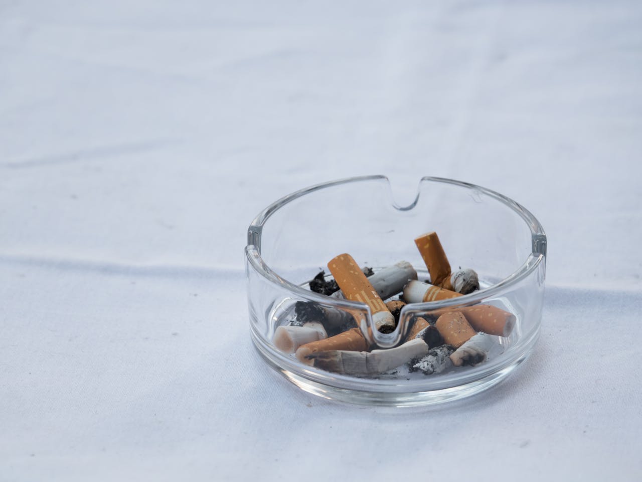 services-02 A clear glass ashtray filled with cigarette butts and ash placed on a white surface.