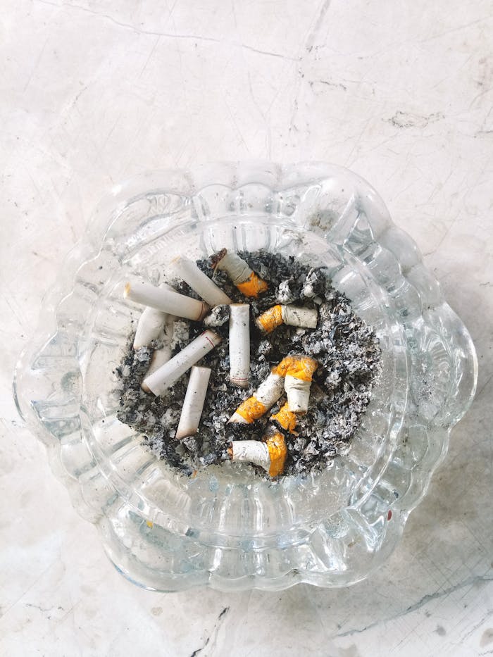 gallery-6 Top view of a glass ashtray filled with cigarette butts and ash on a marbled surface.